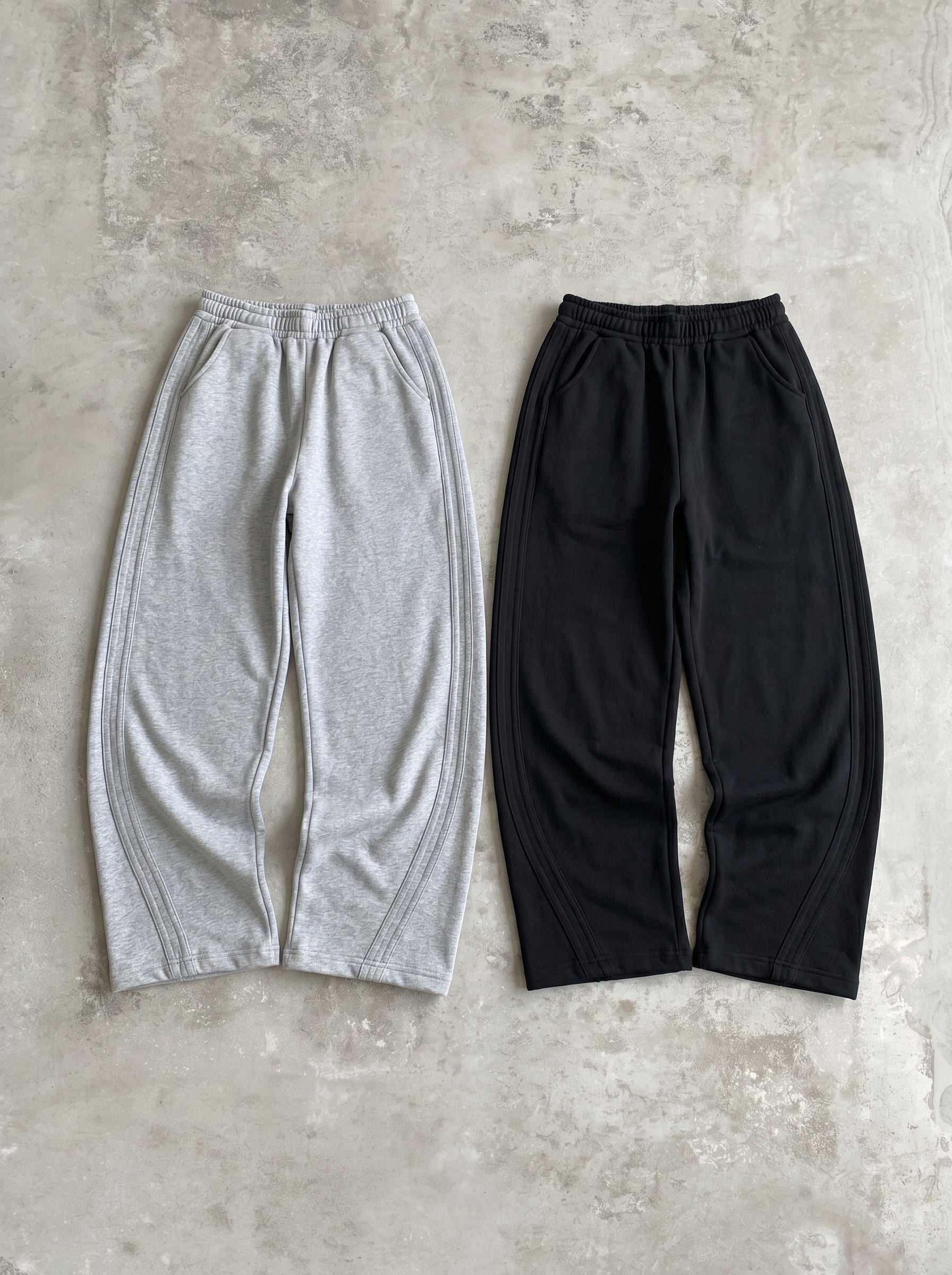 グレーとブラックのワイドスウェットパンツ2色の平置き。前面に脚のラインに沿ったカーブの切り替えステッチ。ワイドシルエットでドローコードウエスト。